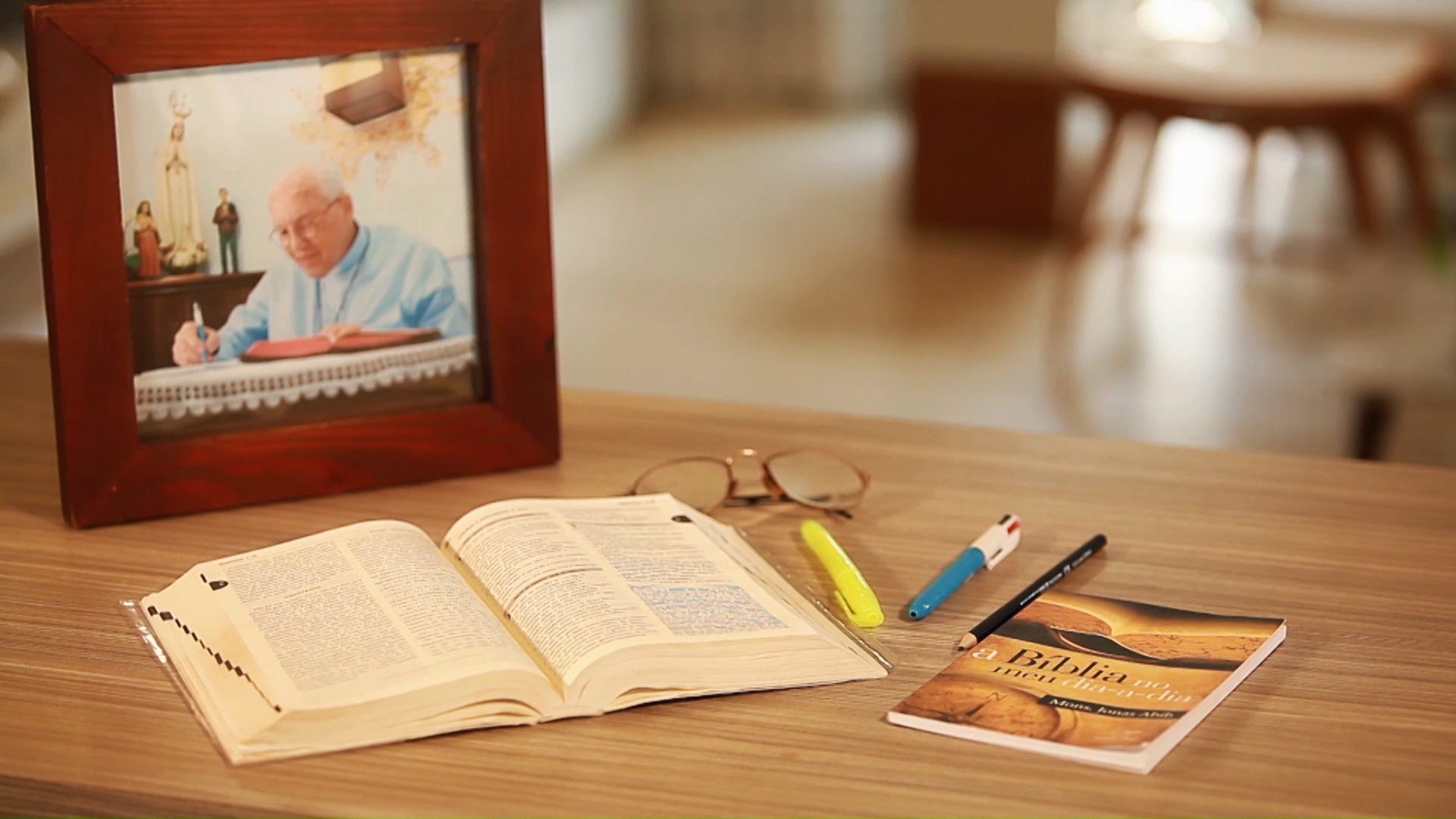 Imagem mostra a Bíblia aberta junto com o livro que ensina o Estudo Bíblico e a foto de Padre Jonas 