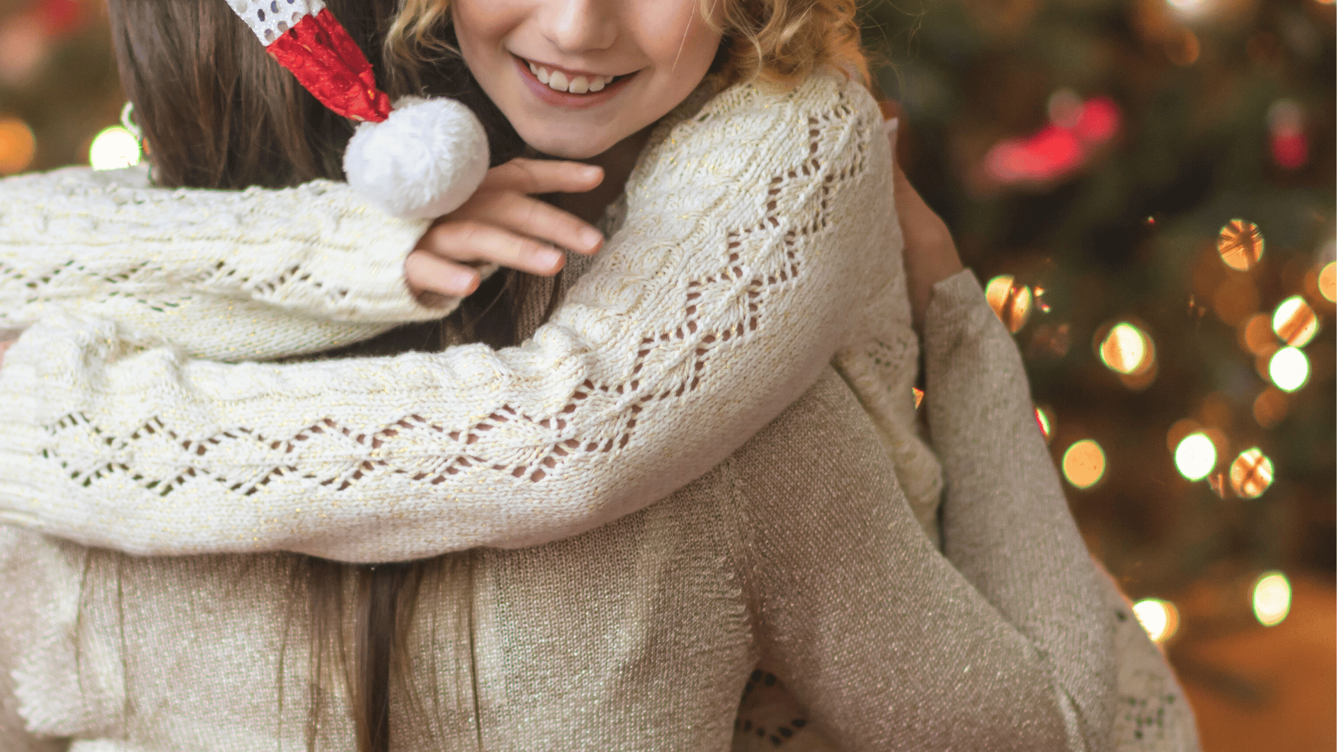 Duas crianças se abraçam sorridentes diante de uma árvore de Natal iluminada, em gesto de carinho e reconciliação