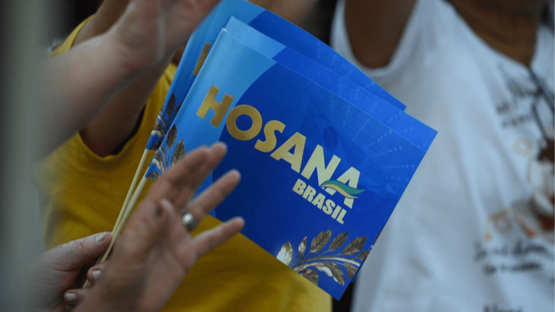 Mãos erguidas de uma mulher seguram uma bandeira azul com o escrito Hosana Brasil