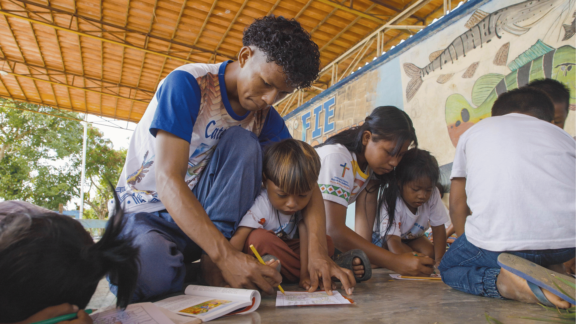Catequista auxiliando crianças em atividades de desenho e catequese em um espaço comunitário