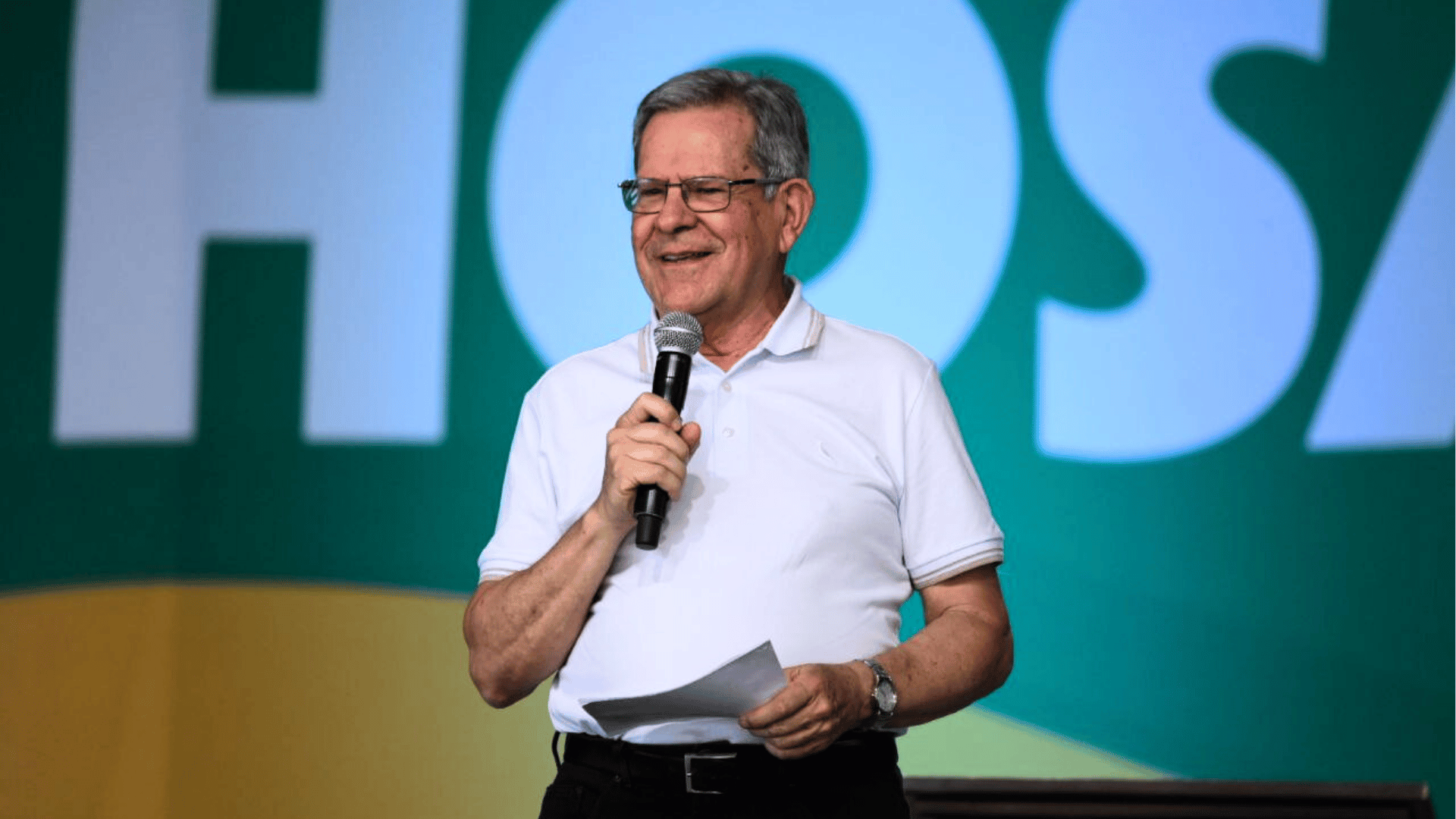 Professor Felipe Aquino está em pé, veste uma camisa branca e segura em suas mãos um microfone e uma folha de papel durante pregação no palco do Hosana Brasil 2025