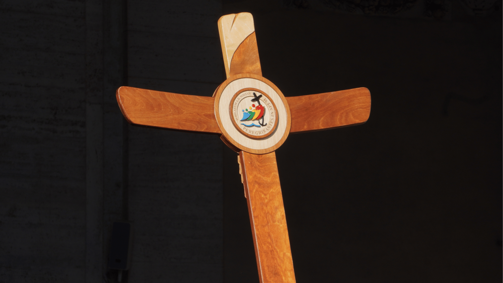 Cruz de madeira tendo ao centro, em formato circular, o logo do Jubileu 2025