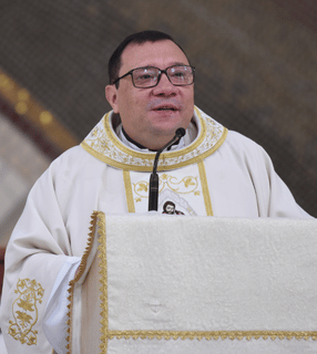Sacerdote conduzindo a homilia durante a celebração, ao lado do ambão litúrgico