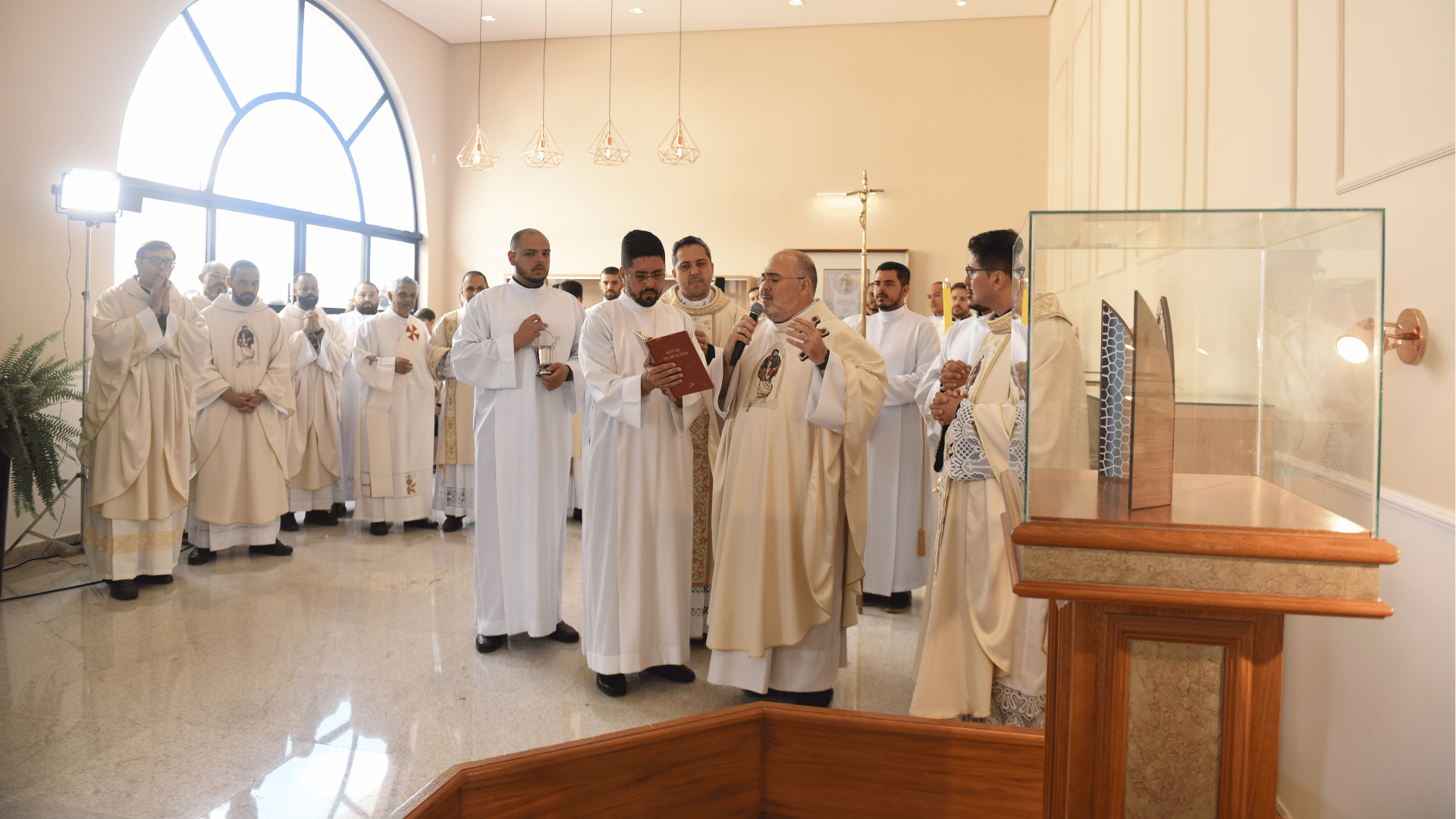 Celebração de inauguração da nova Sala das Graças Alcançadas, com sacerdotes reunidos e rito litúrgico no interior do espaço