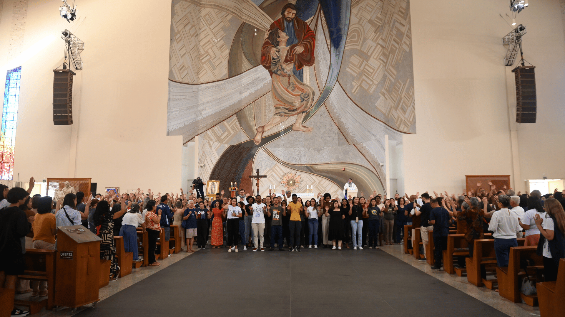 Missionários durante momento de oração Assembleia reunida em igreja durante celebração, com fiéis de braços erguidos diante do altar