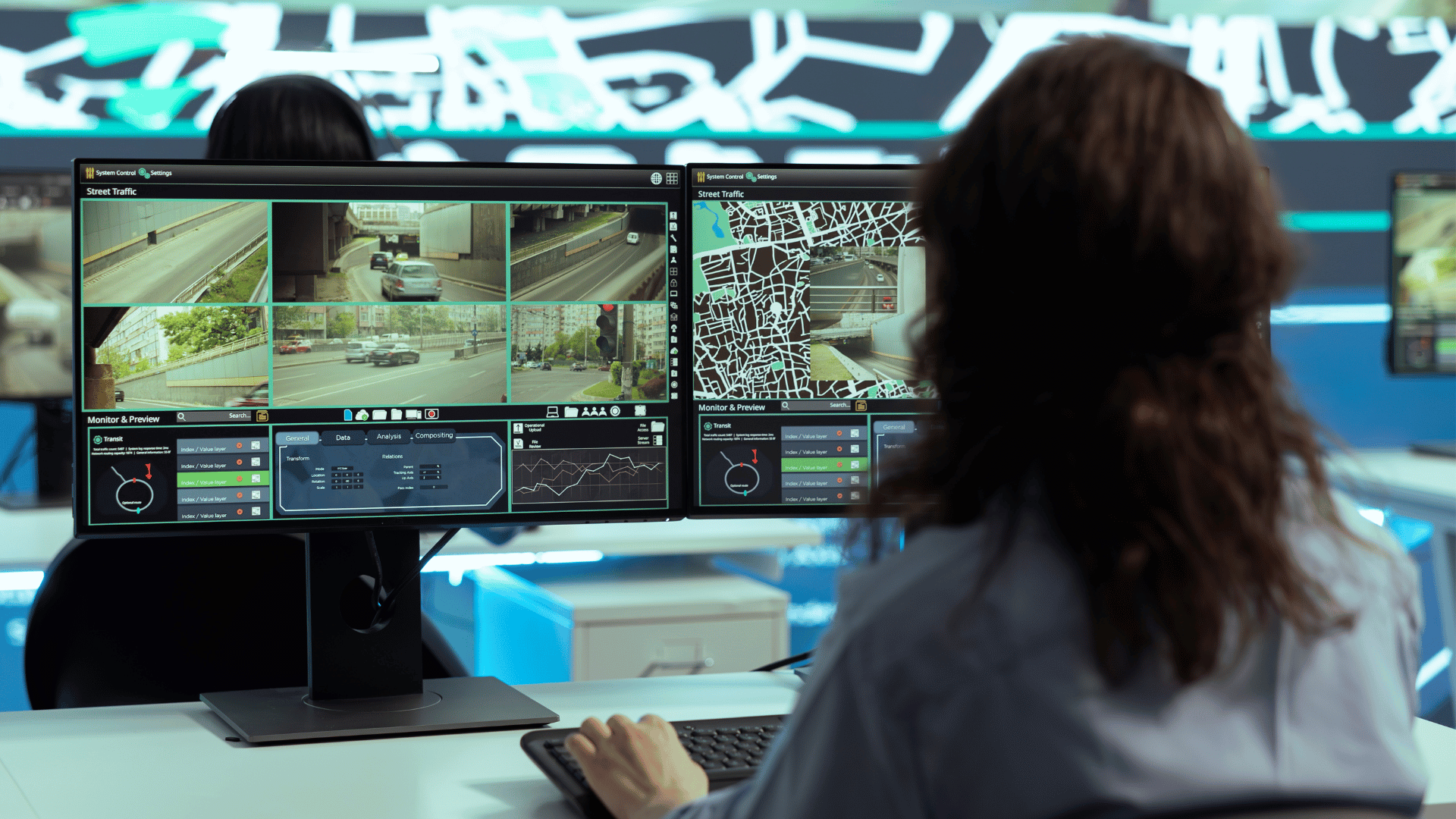 Mulher trabalhando com sistema de monitoramento A imagem ilustra uma mulher utlizando um computador, olhando para monitores que exibem as imagens gravads por câmera de segurança e outras informações ligadas a um sistema de monitoramento.