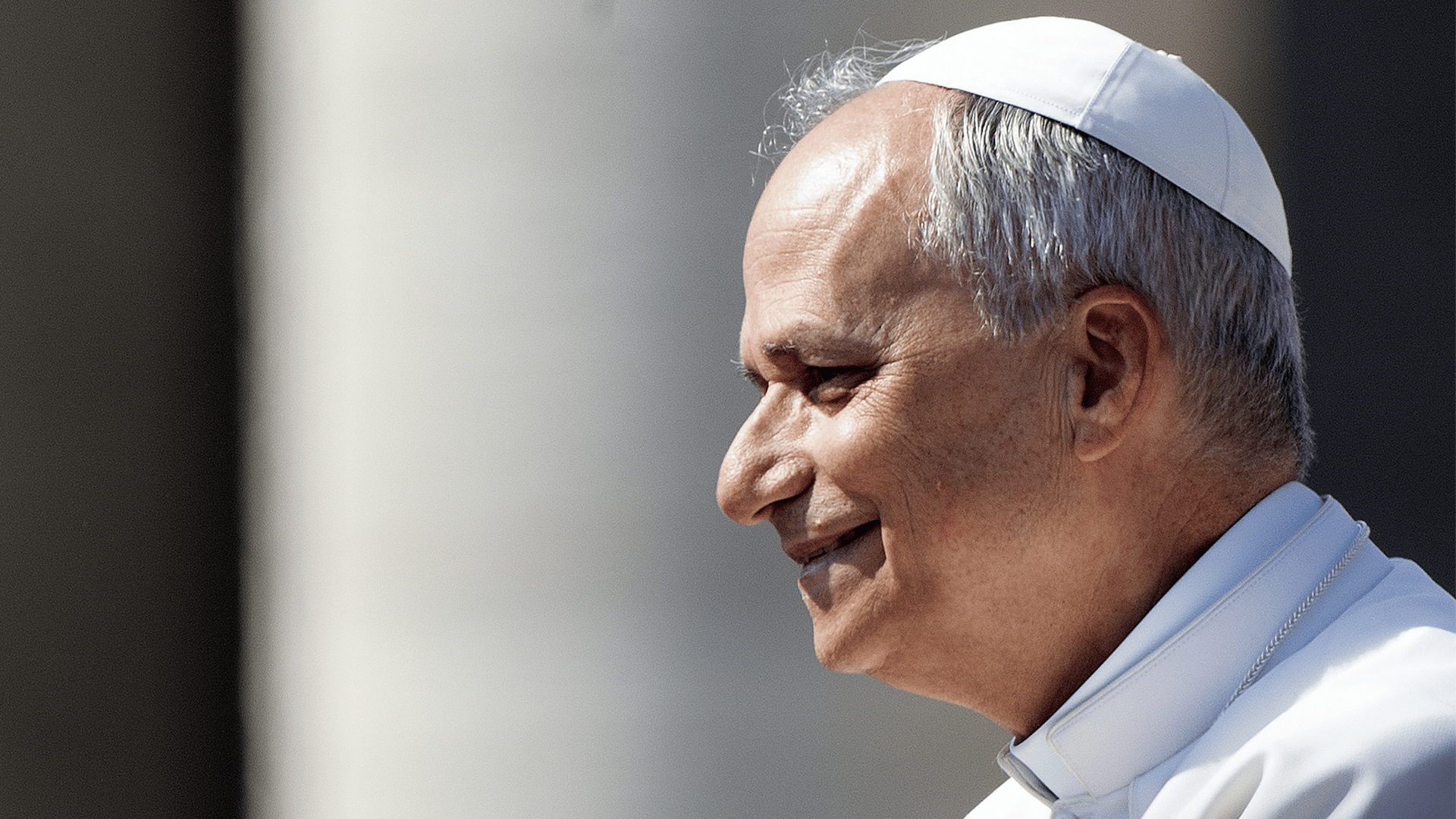 A imagem ilustra o Papa Leão XIV com suas habituais vestes pontifícias, de perfil e um leve sorriso.