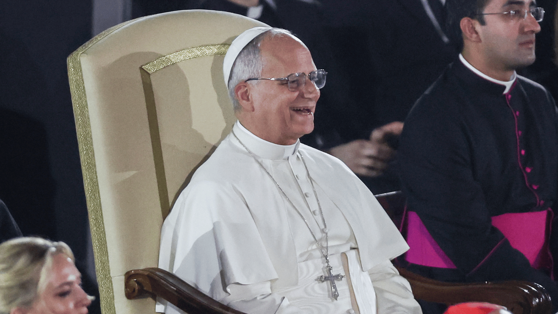 Papa Leão XIV sorri durante apresentação no Concerto com os Pobres A imagem mostra o Papa Leão XIV sorrindo, sentado em sua cadeira, enquanto acompanha uma apresentação musical na Sala Paulo VI.