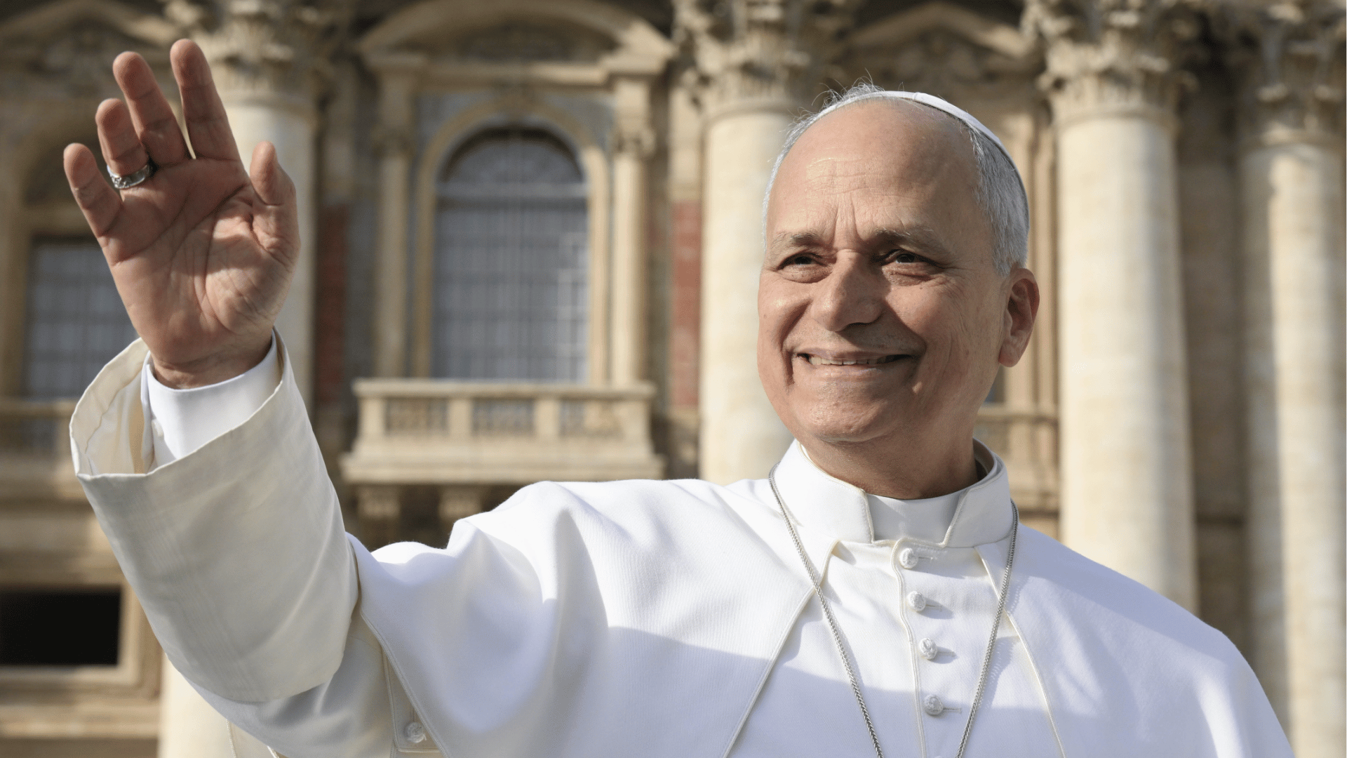 Papa vestido de branco acena sorridente aos fiéis, com a Basílica de São Pedro ao fundo 