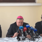 três bispos aparecem sentados à uma mesa sobre as quais há microfones de diversos veículos de comunicação