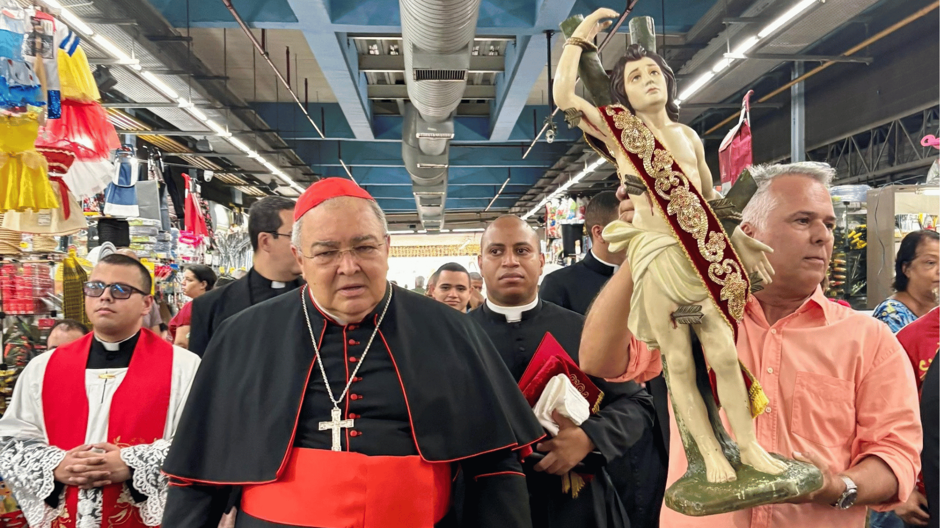 Imagem de São Sebastião é conduzida em procissão por fiéis em um corredor comercial; à frente, o arcebispo do Rio de Janeiro