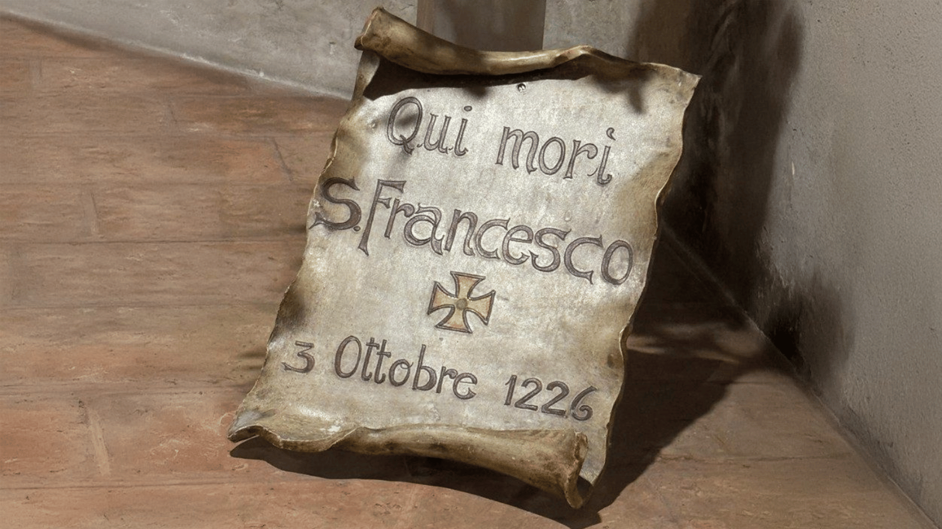A imagem ilustra uma inscrição onde está escrito "Qui mori S. Francesco - 3 ottobre 1226" (em tradução livre, "Aqui morre São Francisco - 3 de outubro de 1226).