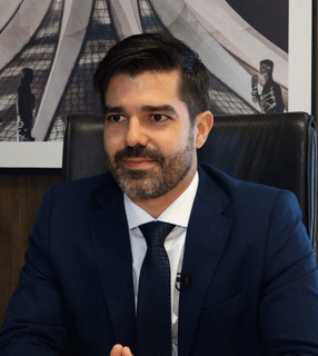 Lucas Furtado sentado à mesa em ambiente profissional, com expressão serena e fundo institucional.