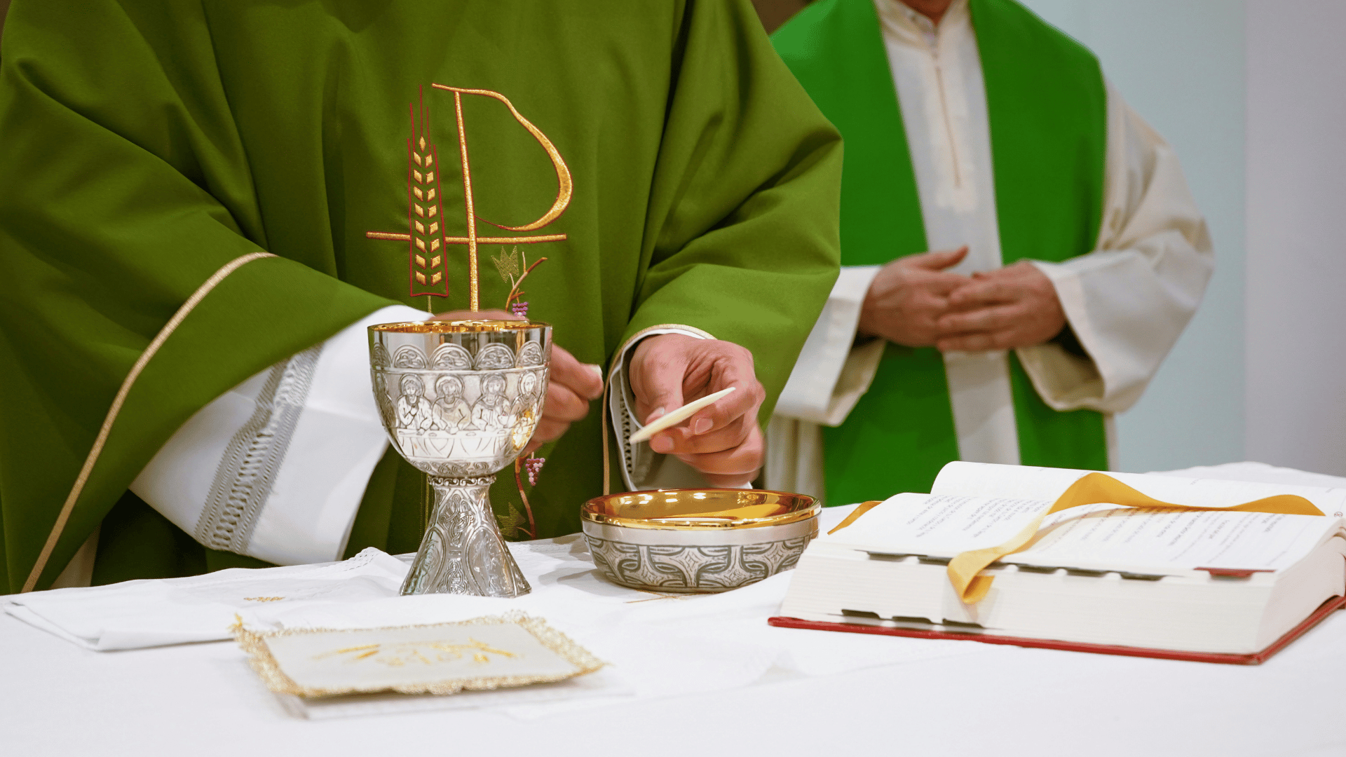 A imagem ilustra objetos litúrgicos (cálice, âmbula, Missal, entre outros) sobre um altar durante a celebração da Missa. Ao fundo, vê-se dois padres com vestes litúrgicas verdes.