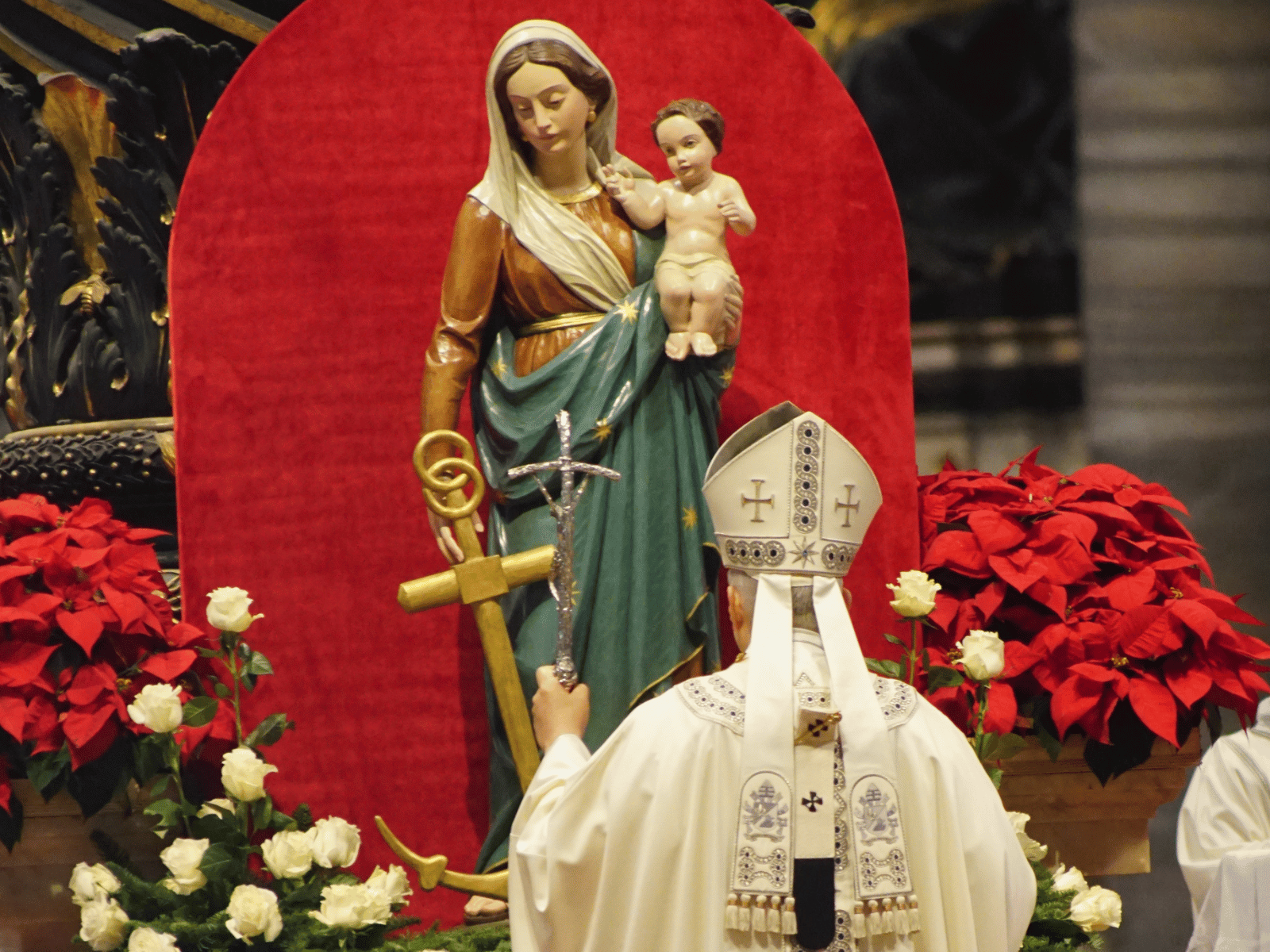 A imagem ilustra o Papa Leão XIV, de costas, observando uma imagem de Nossa Senhora da Esperança. O Pontífice usa vestes litúrgicas brancas e traz a cruz processional em sua mão esquerda. A imagem de Nossa Senhora traz o Menino Jesus no braço esquerdo e uma âncora dourada na mão direita.