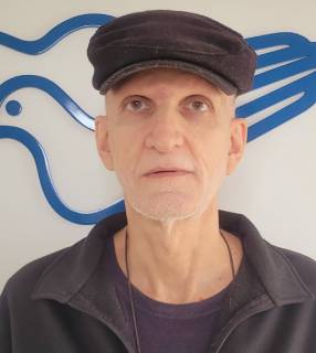 homem com boina em frente ao logo da Canção Nova 