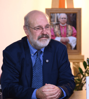 Silvonei José e o Papa Leão XIV A imagem ilustra um homem de pele branca, com cabelos grisalhos ralos e barba grisalha, vestido com um paletó azul marinho. Ao fundo vê-se um quadro com uma foto do Papa Leão XIV.