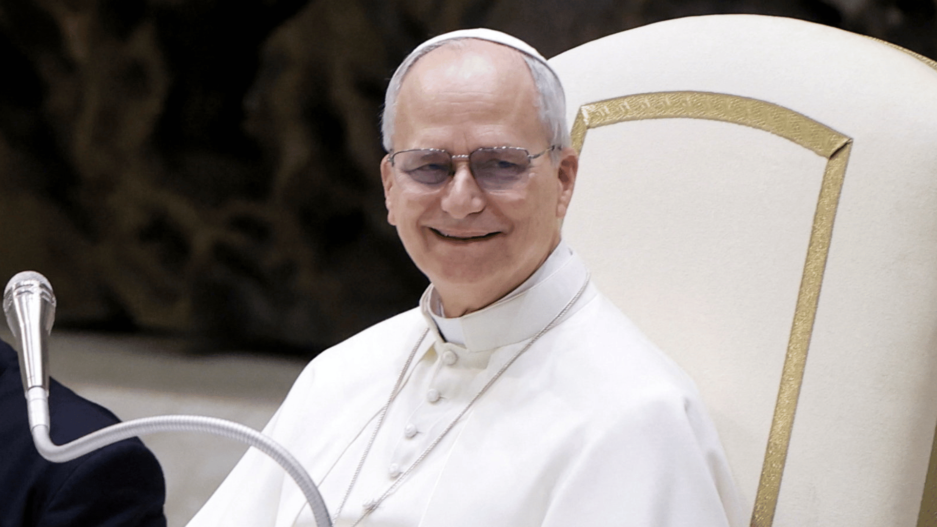 A imagem ilustra o Papa Leão XIV com suas habituais vestes pontifícias, sorrindo, sentado em sua cadeira durante nma Audiência Geral na Sala Paulo VI.