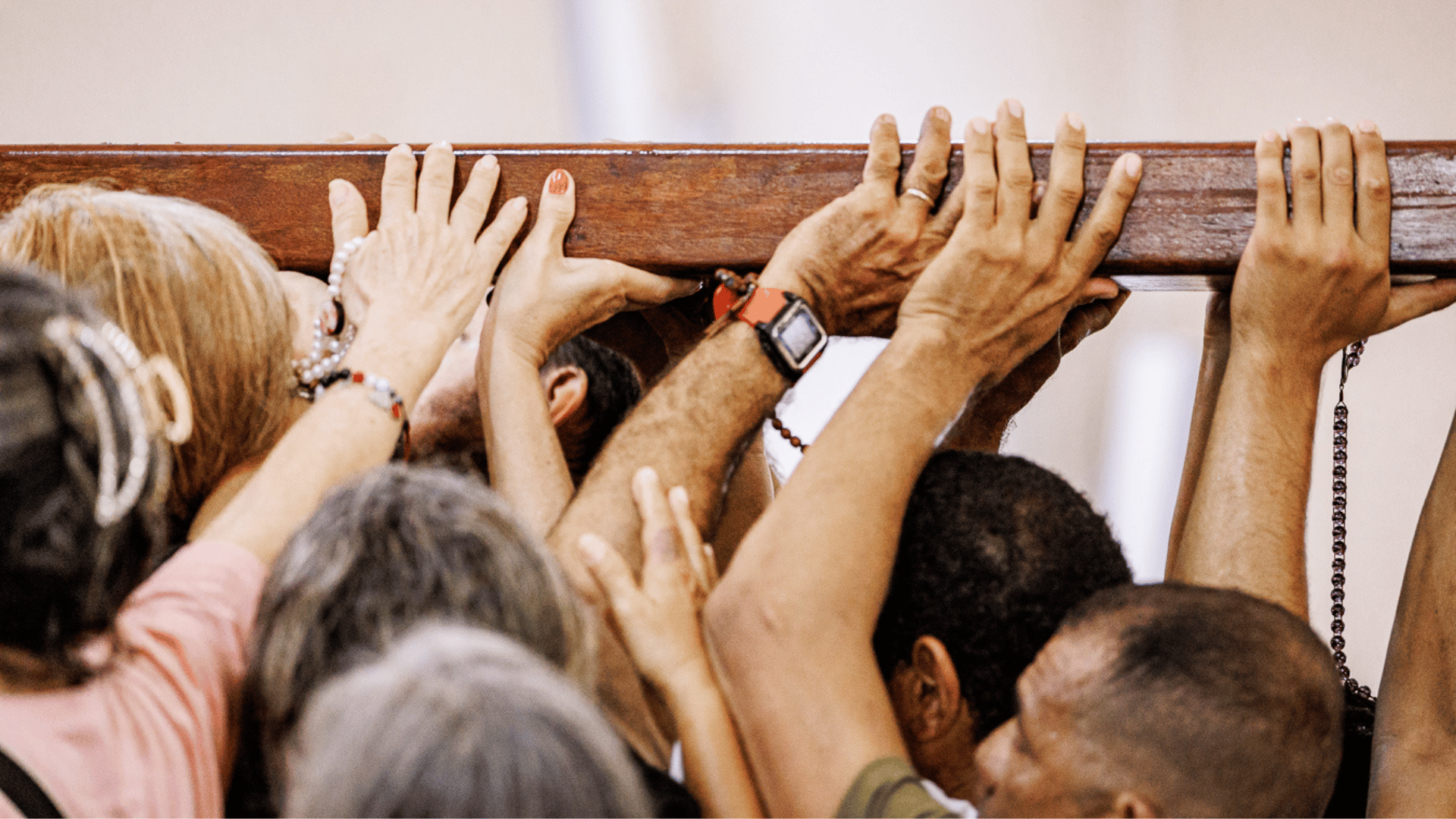 A imagem ilustra, em detalhe, várias mãos carregando uma cruz durante uma caminhada.