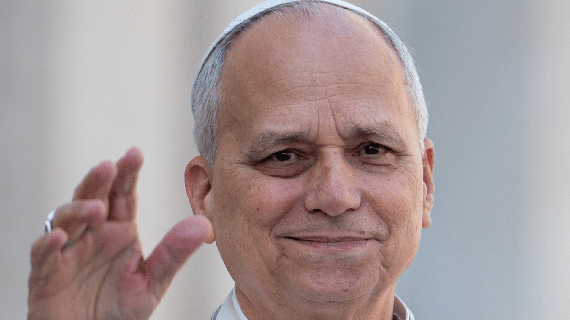 Papa Leão XIV sorrindo e acenando com a mão, vestindo batina branca e solidéu.