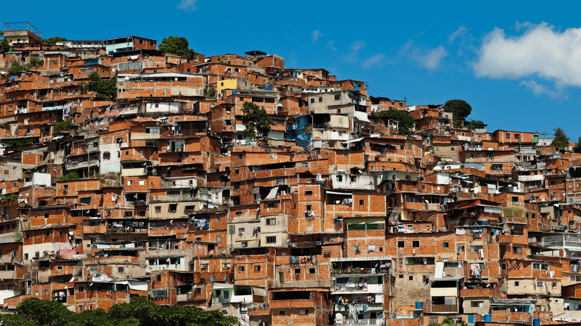 Comunidade urbana com casas de tijolo aparentes construídas de forma densa em encosta, sob céu azul.