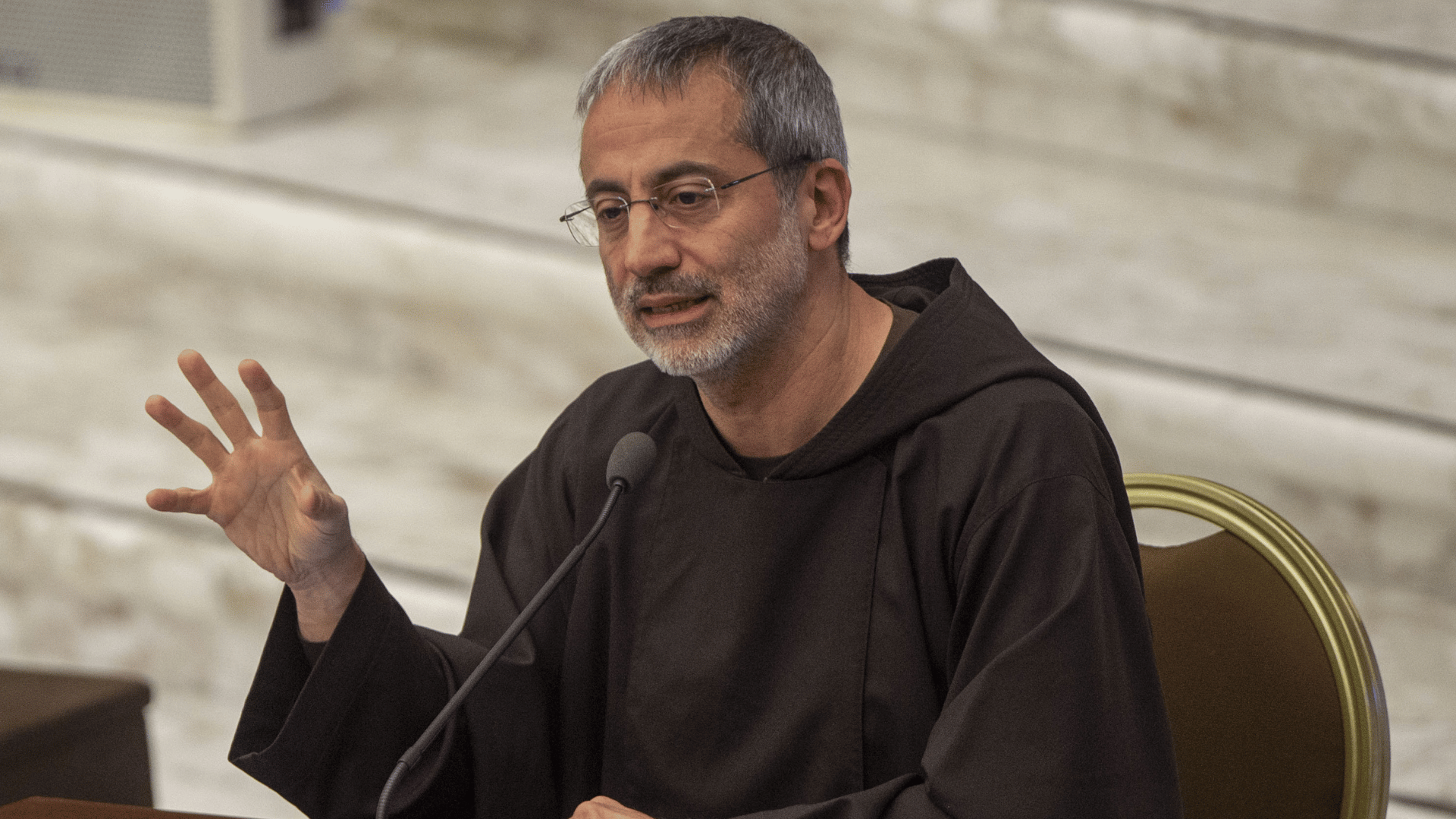 Padre Roberto Pasolini de hábito marrom fala ao microfone, durante pregação na Sala Paulo VI