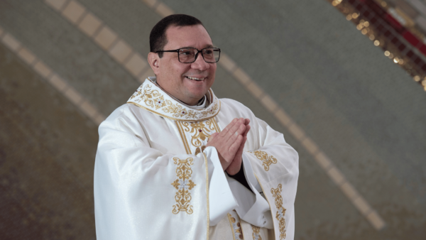 Padre Wagner Ferreira aparece sorrindo, com as mãos unidas e vestes litúrgicas brancas