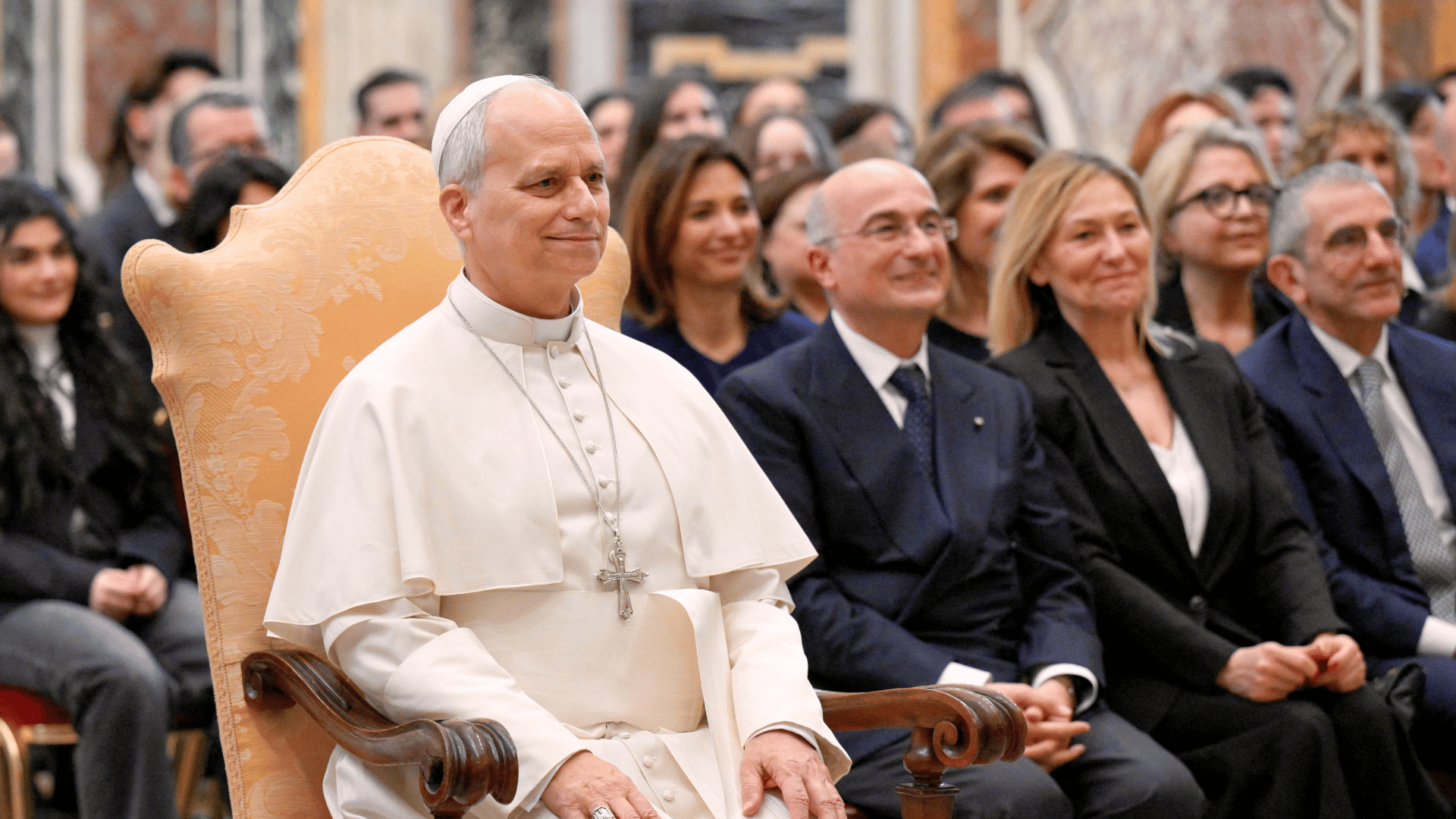 Papa sentado em cadeira durante audiência com convidados em salão do Vaticano