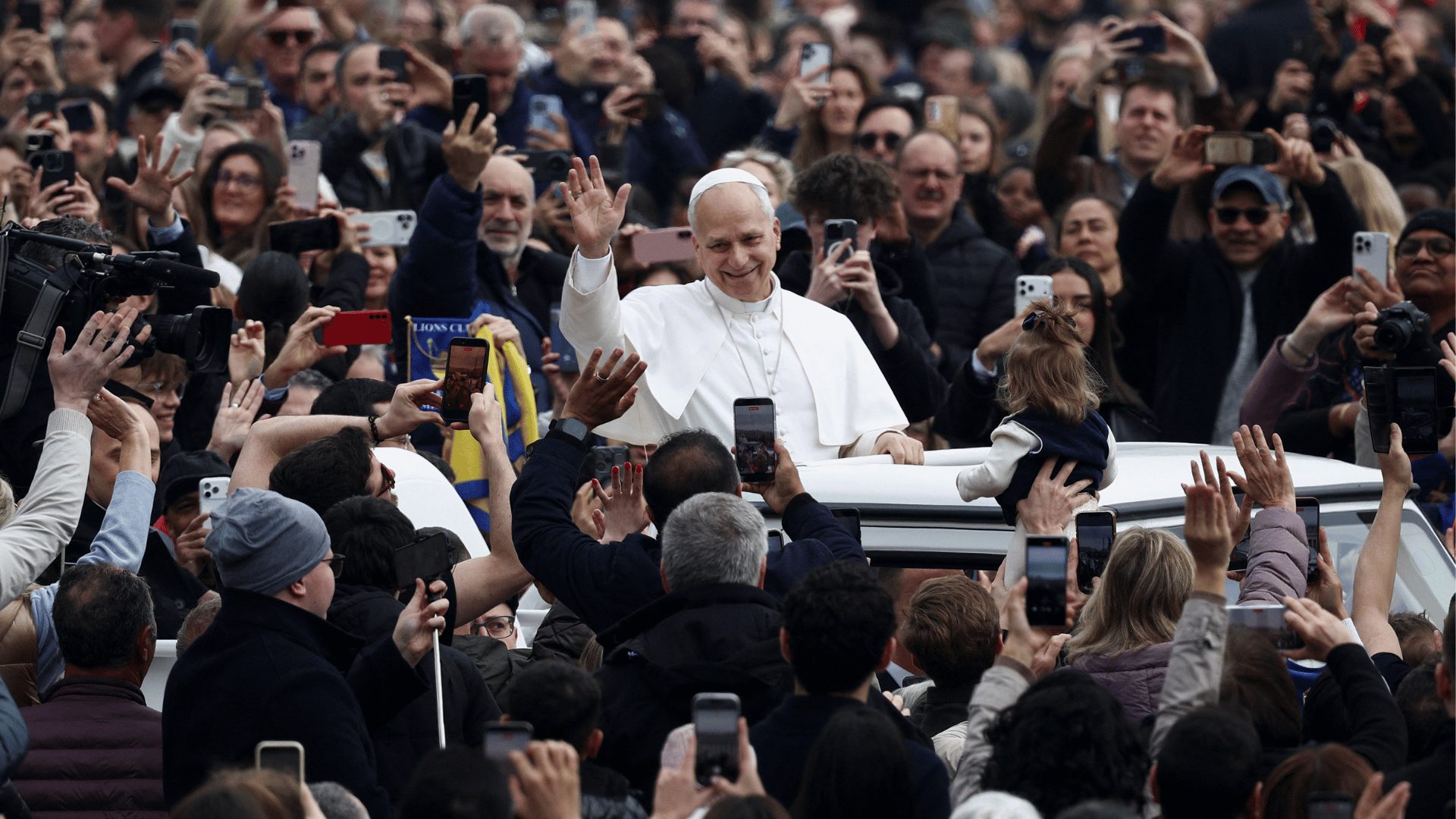 Papa Leão XIV passa em meio aos fiéis no papamóvel A imagem ilustra o Papa Leão XIV no papamóvel, com suas habituais vestes pontifícias e o braço direito erguido em gesto de saudação, passando em meio a uma multidão de fiéis na Praça São Pedro.