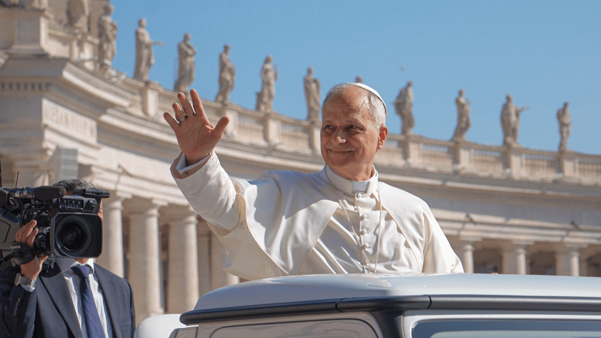 Papa Leão XIV com suas habituais vestes pontifícias e o braço direito erguido em gesto de saudação.