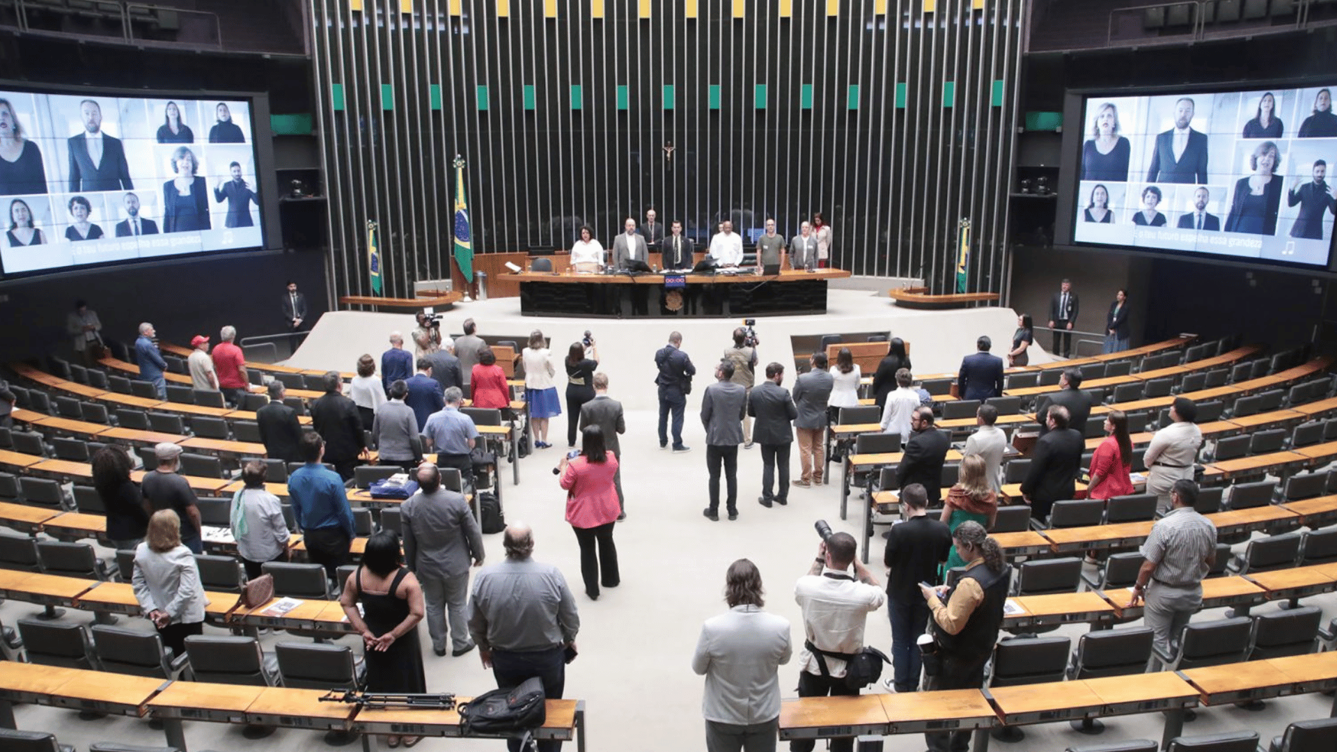 Plenário da Câmara dos Deputados com parlamentares e convidados em pé durante sessão solene.
