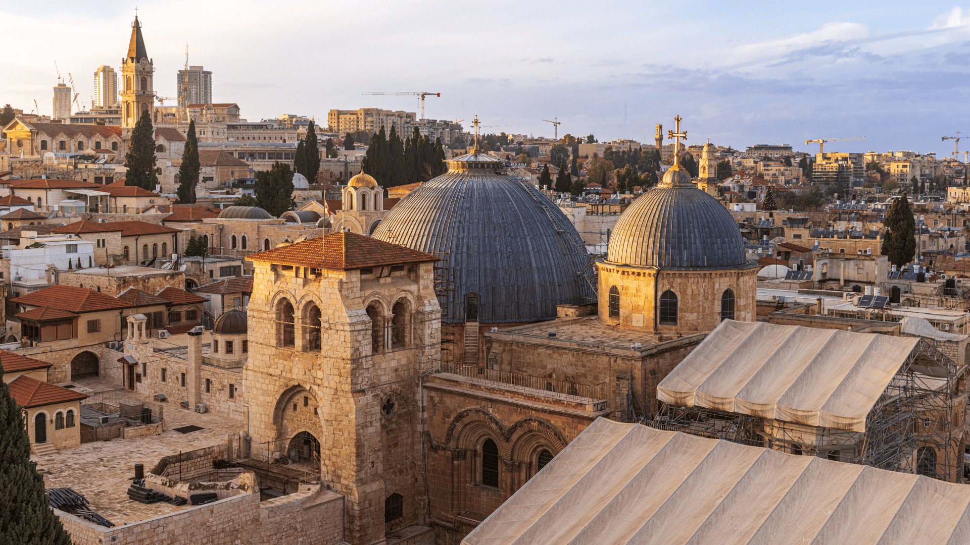 Vista aérea da cidade de Jerusalém com destaque para a Igreja do Santo Sepulcro, com cúpulas e construções históricas ao redor.