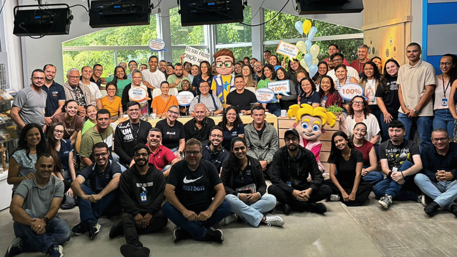 Missionários e colaboradores da Canção Nova reunidos no estúdio do Sorrindo pra Vida, com cartazes celebrando o 100% do Projeto Dai-me Almas.