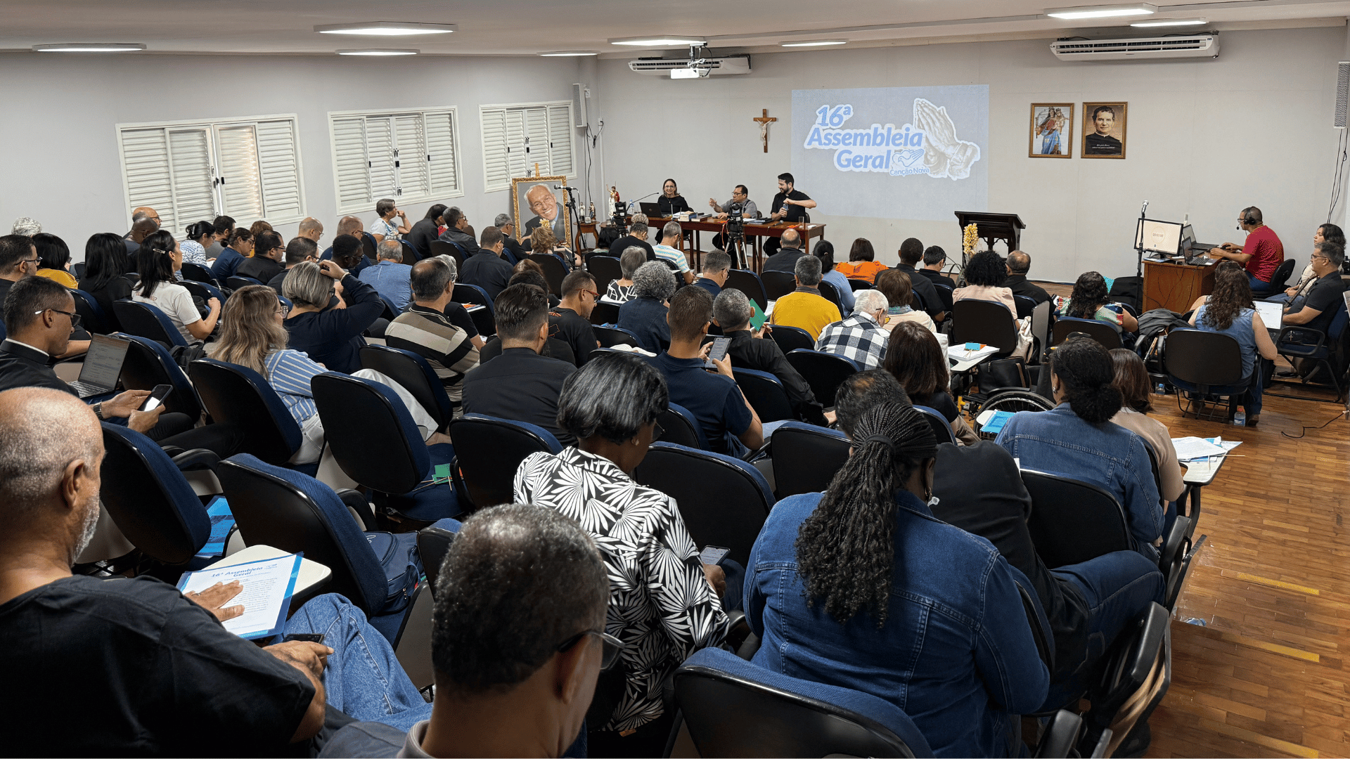 A imagem ilustra um grupo de pessoas reunido em um auditório.