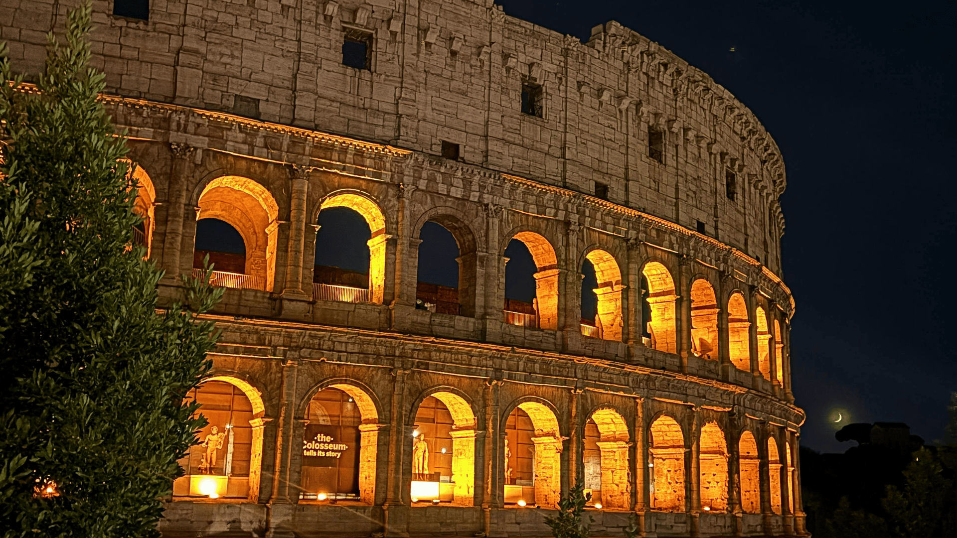 Vista noturna do Coliseu de Roma iluminado em tons dourados, com seus arcos históricos em destaque contra o céu escuro.