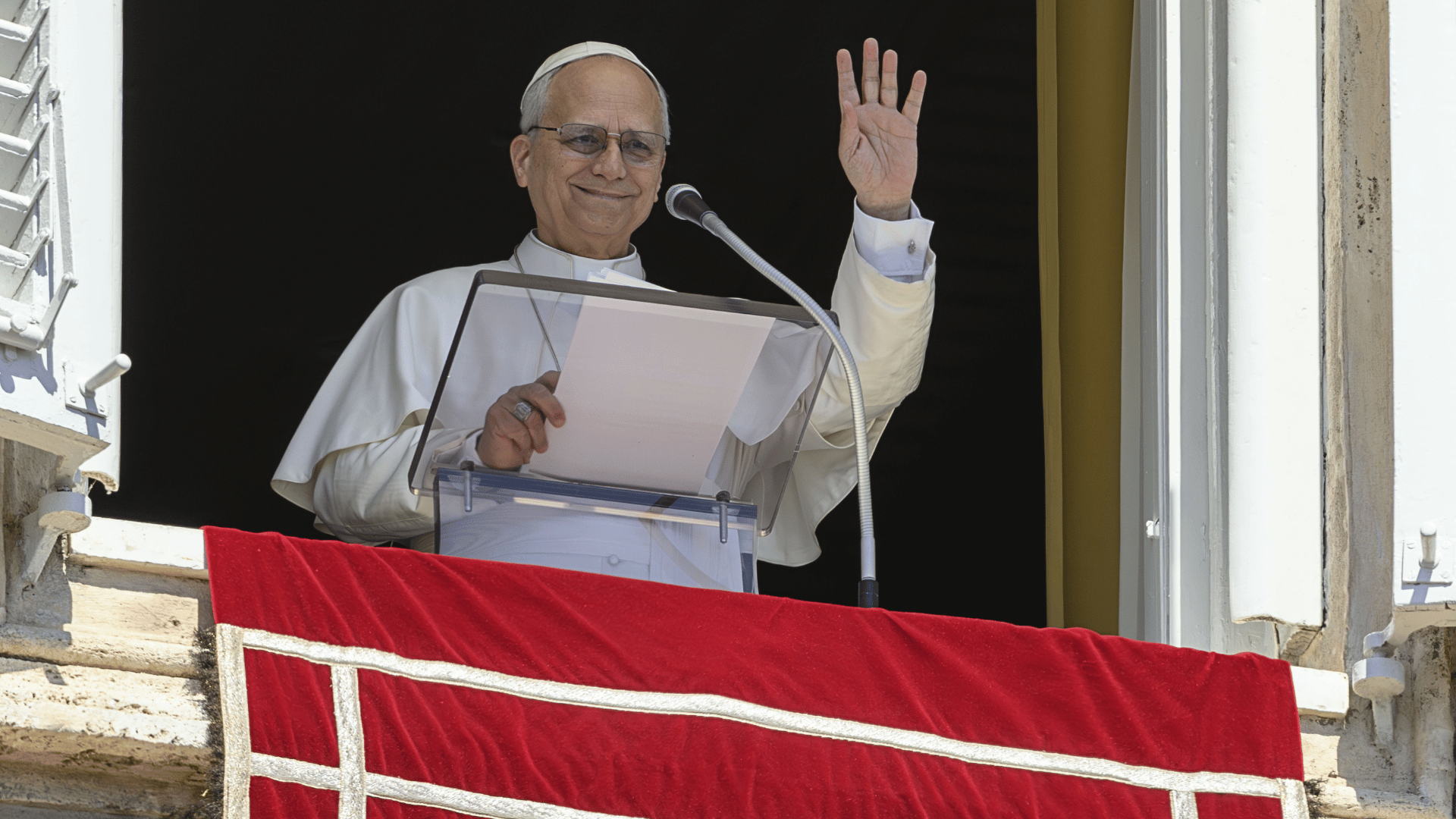 O Papa Leão XIV aparece em uma janela com suas habituais vestes brancas acenando com sua mão esquerda