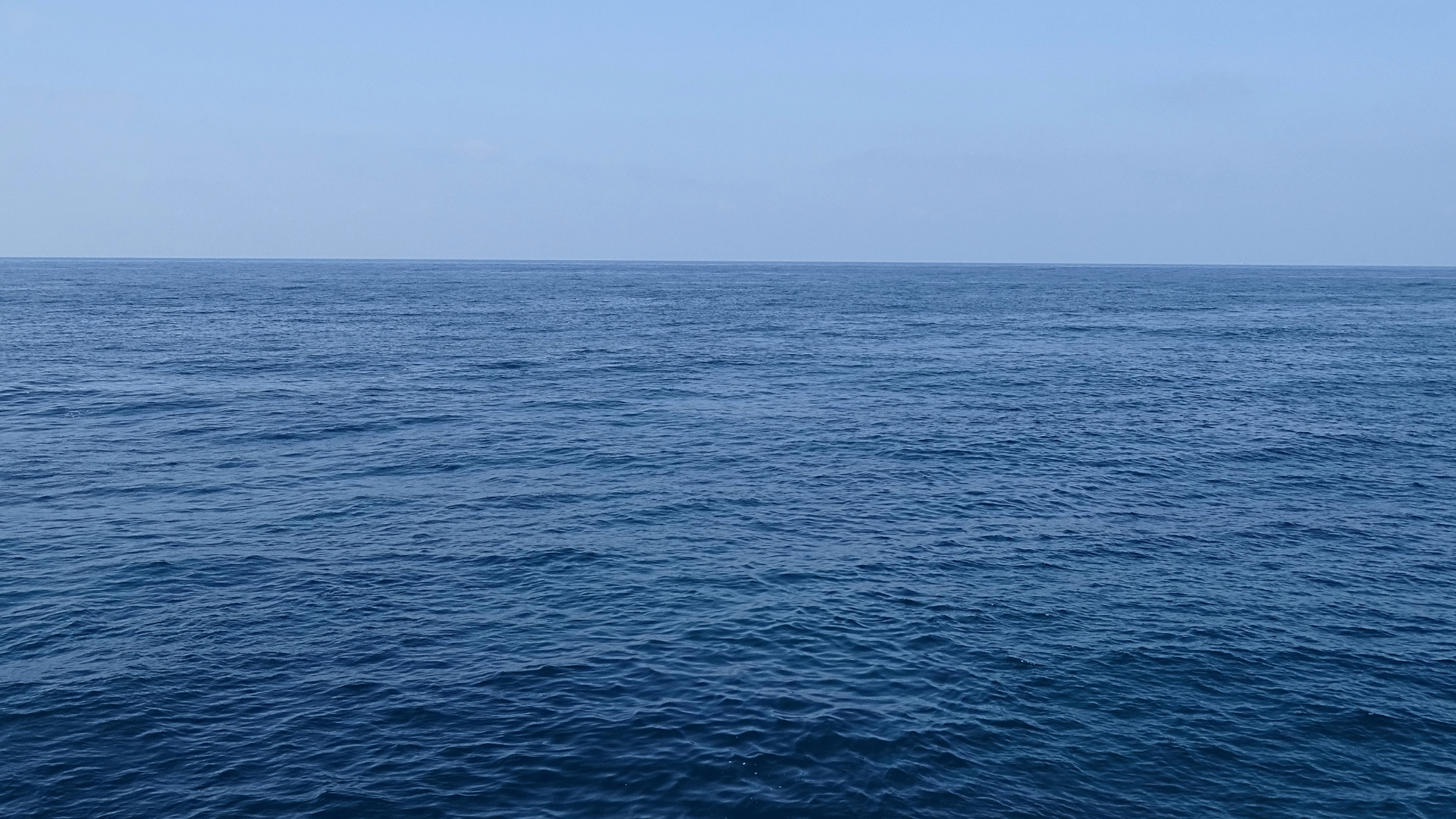 Vista do mar aberto com águas calmas e horizonte ao fundo sob céu claro.