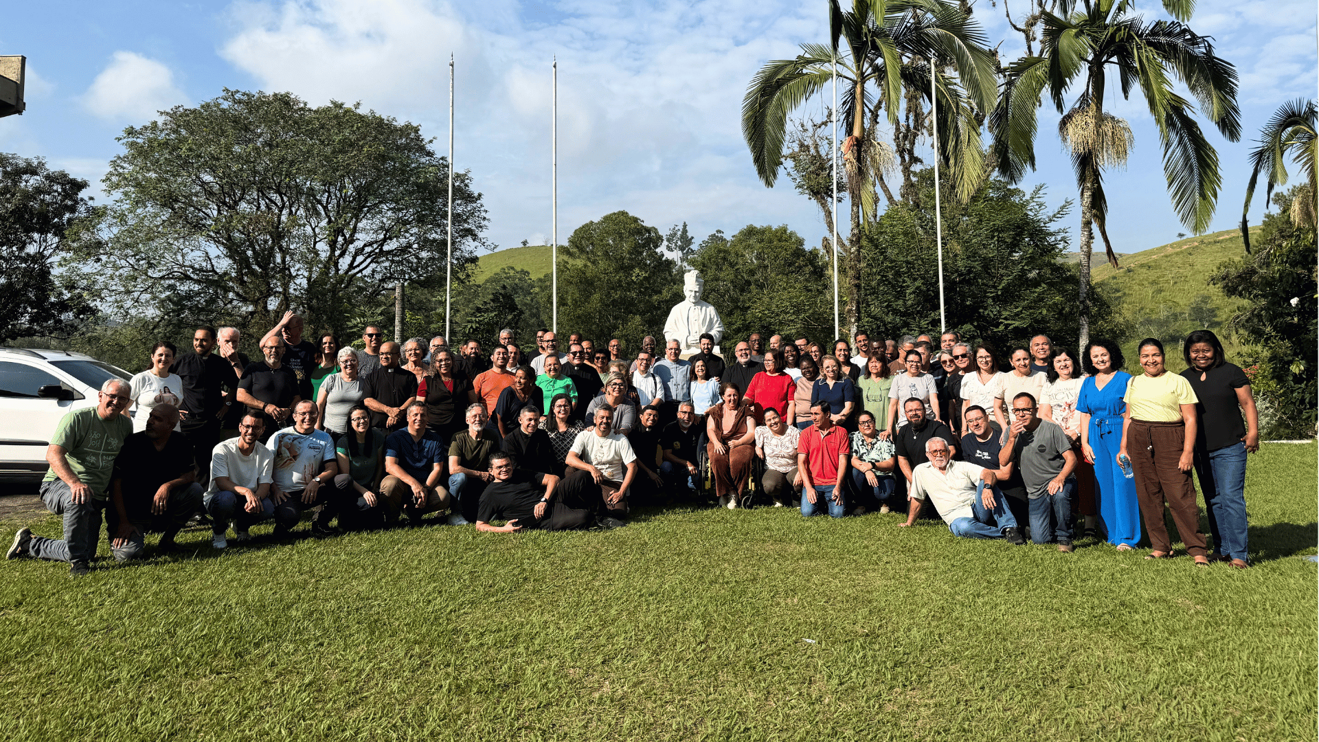 Missionários reunidos durante a Assembleia Geral da Canção Nova, em área externa com gramado e árvores, diante da imagem de Dom Bosco
