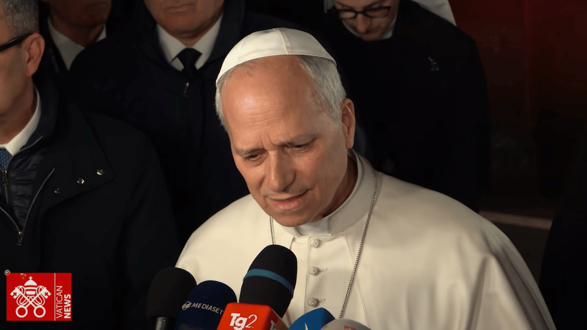 O Papa Leão XIV aparece com suas tradicionais vestes brancas falando a vários microfones que estão posicionados diante dele
