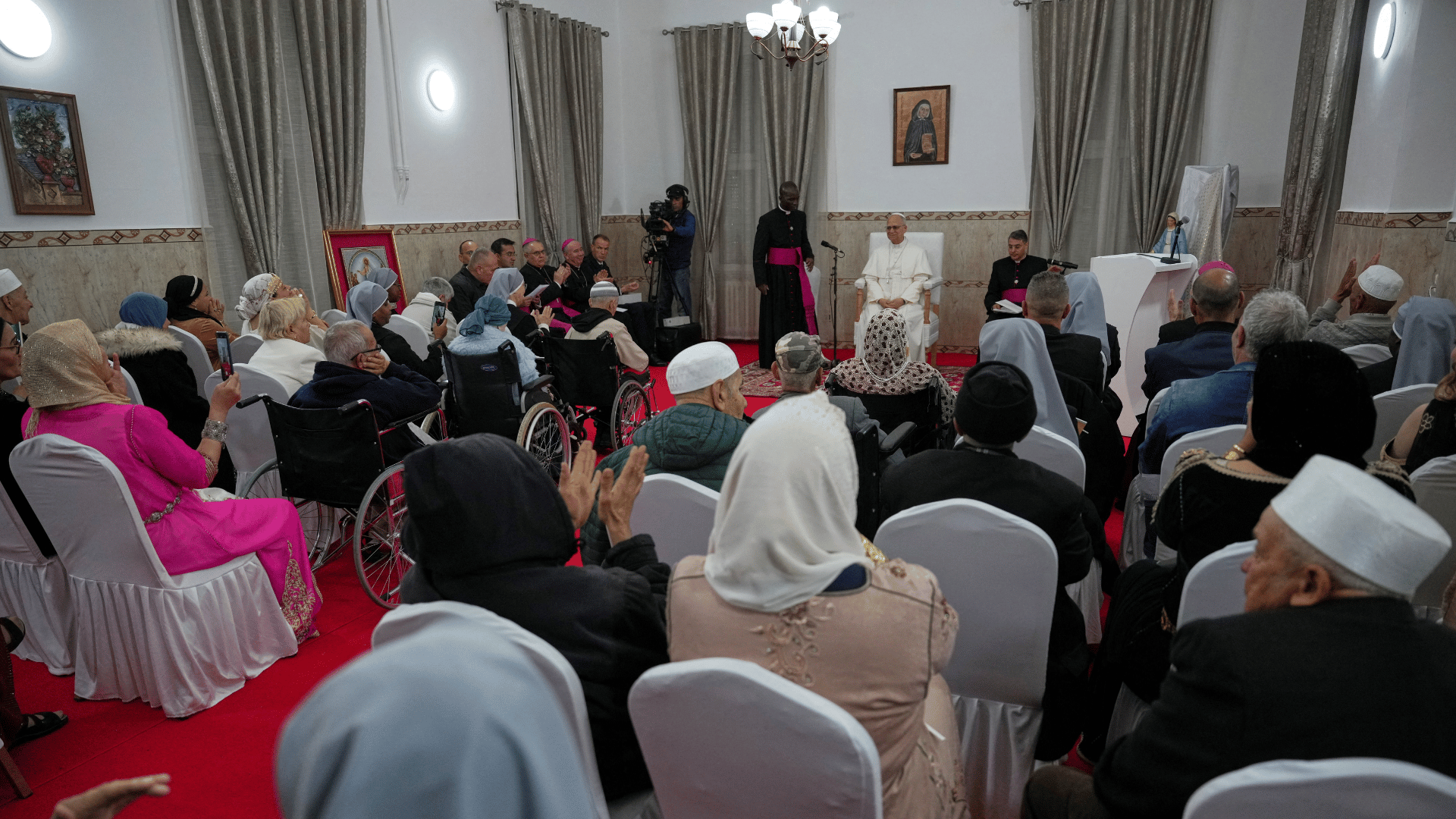 Papa Francisco encontra-se com pessoas idosas e religiosos em uma casa de acolhimento na Argélia, sentado à frente de um grupo reunido em uma sala.
