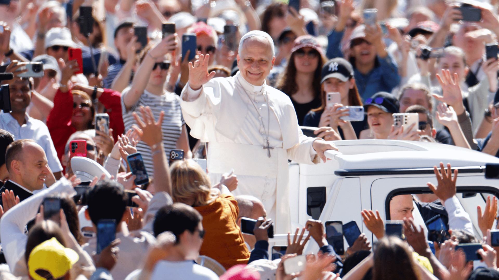 A imagem ilustra o Papa Leão XIV, com suas habituais vestes pontifícias, em pé no papamóvel, cercado por fiéis.
