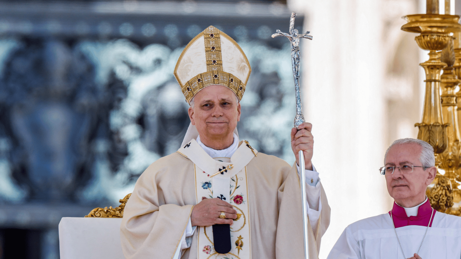 Papa Leão XIV na primeira Missa de Páscoa de seu pontificado A imagem ilustra o Papa Leão LIX com paramentos litúrgicos brancos com detalhes dourados. Ele tem a mão direita sobre o peito enquanto segura, com a mão esquerda, a férula papal.