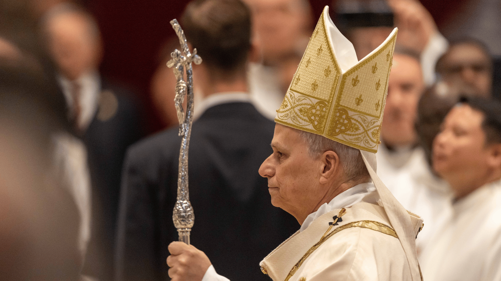 A imagem ilustra o Papa Leão XIV de perfil, paramentado com vestes litúrgicas brancas com detalhes dourados e carregando a férula papal com a mão esquerda.