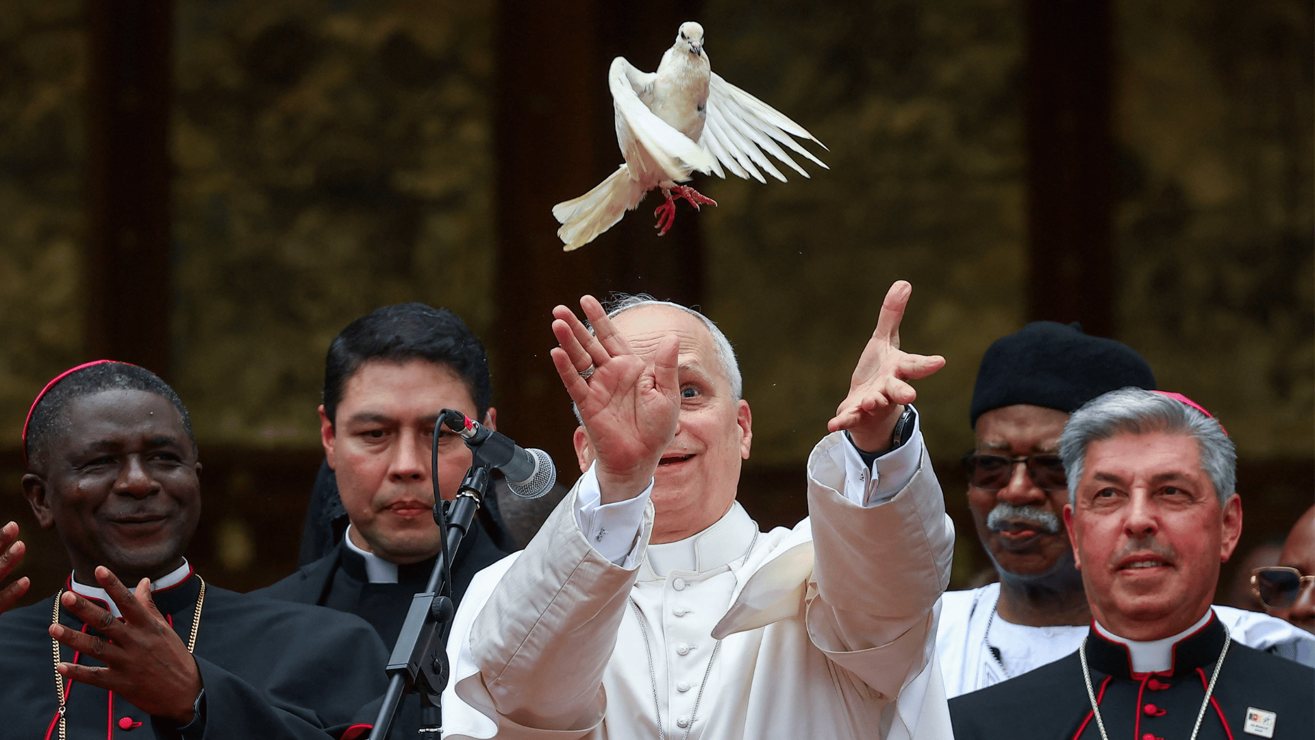A imagem ilustra o Papa Leão XIV soltando uma pomba branca, que voa acima de sua cabeça, cercado por outros religiosos.