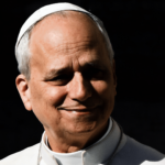 Papa sorrindo, vestido de branco, com solidéu e expressão serena, sobre fundo escuro.