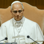 O Papa Leão XIV aparece com suas habituais vestes brancas sentado a uma mesa diante de dois microfones