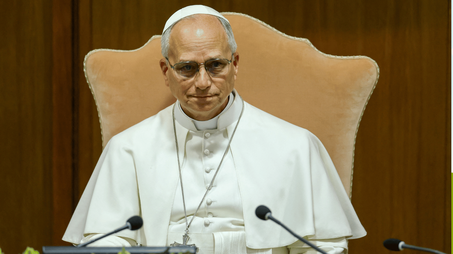 O Papa Leão XIV aparece com suas habituais vestes brancas sentado a uma mesa diante de dois microfones