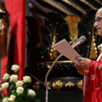 O Papa Leão XIV aparece paramentado com vestes litúrgicas vermelhas e fala ao microfone segurando um papel em suas mãos