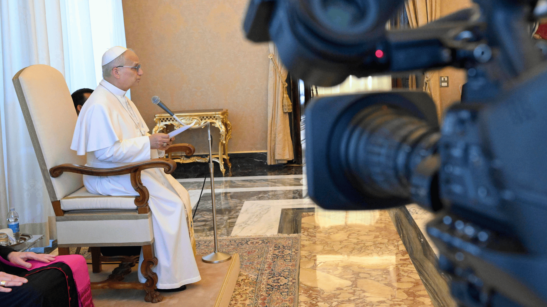 Papa Leão XIV durante audiência no Vaticano nesta sexta-feira, 22 A imagem ilustra o Papa Leão VIX, sentado, lendo um discurso diante de um microfone. Em primeiro plano e desfocada, vê-se uma câmera de televisão.