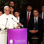Papa Leão XIV discursa em púlpito da Universidade Sapienza de Roma diante de estudantes e autoridades acadêmicas durante visita pastoral.